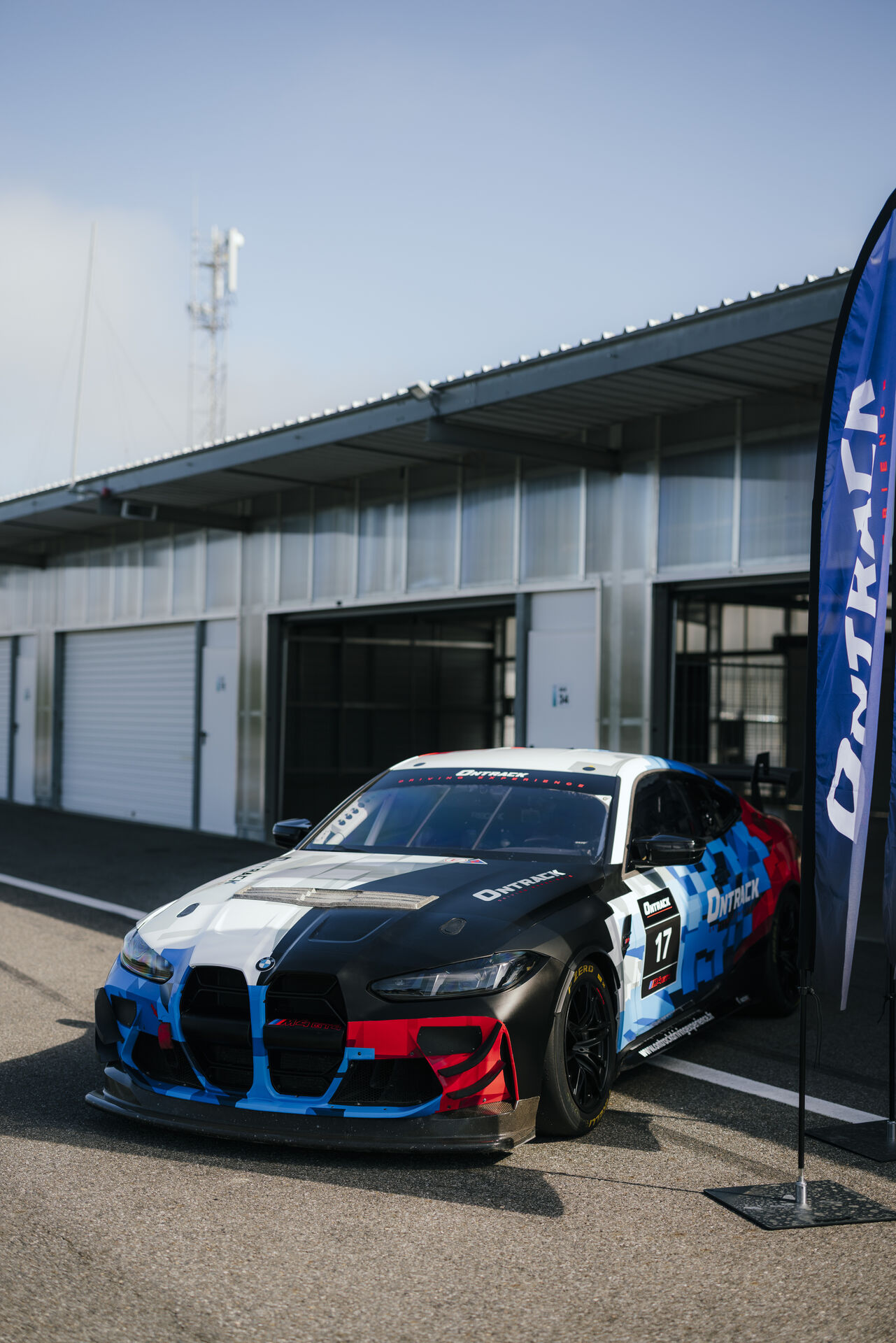 BMW M4 GT4 EVO ONTRACK dans les paddocks avec drapeau ONTRACK