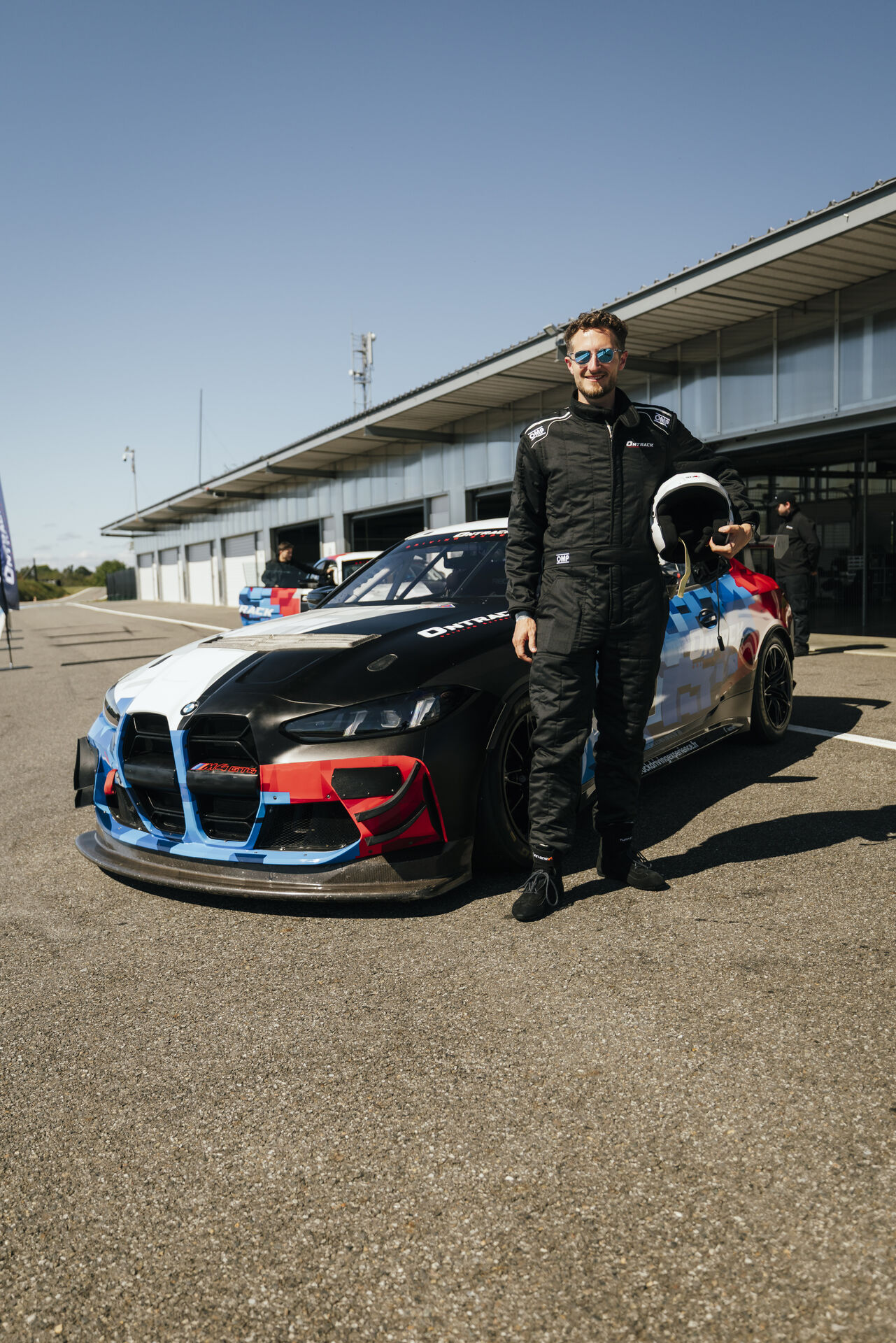 Pilote ONTRACK en combinaison devant une BMW M4 GT4 sur circuit